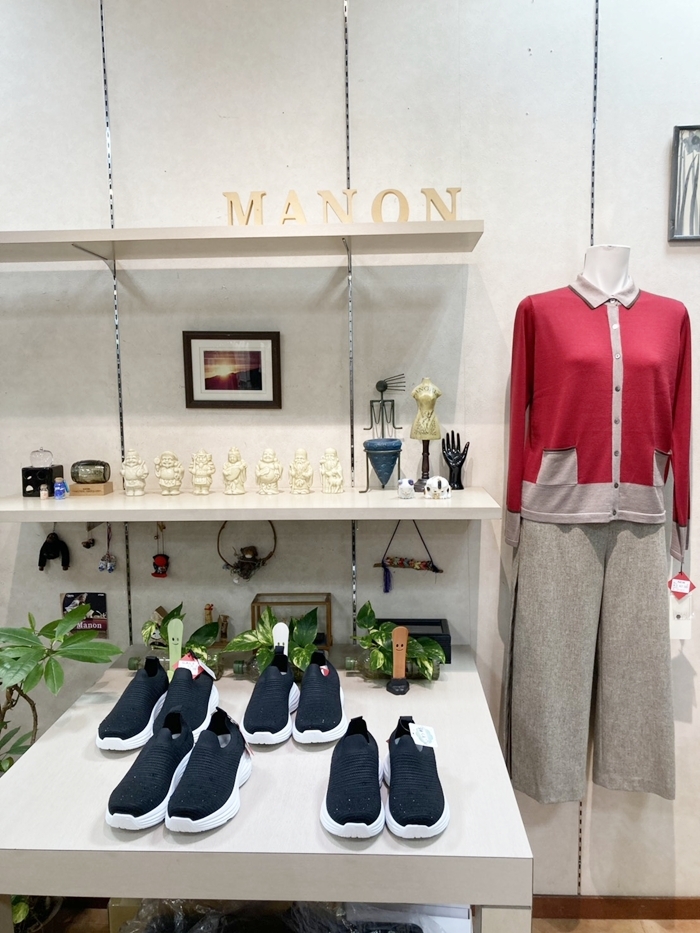 赤とグレーの配色が特徴の襟付きトップスとグレーのパンツ、店頭に並ぶ黒色のシューズ